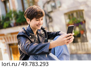 A joyful young person smiles while using their smartphone outdoors in a vibrant urban setting, surrounded by stunning, colorful scenery that creates a lively and energetic atmosphere. A cheerful young individual is actively engaged with their smartphone in a lively urban setting. Стоковое фото, агентство Ingram Publishing / Фотобанк Лори