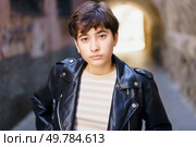 In an urban environment, a young woman dressed in a sleek leather jacket showcases her fashionable and contemporary style as she poses with confidence and attitude, capturing the essence of modernity. A Confident Young Woman Dressed in a Leather Jacket Poses Against an Urban Background. Стоковое фото, агентство Ingram Publishing / Фотобанк Лори