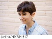 A cheerful and vibrant young woman with short hair beams a warm smile while dressed in a casual blue denim shirt set against a light, textured brick background that enhances her inviting presence. A Smiling Young Woman with Short Hair Dressed in a Casual Blue Shirt Appearing Happy and Cheerful. Стоковое фото, агентство Ingram Publishing / Фотобанк Лори