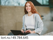 A young woman with long red hair sits outdoors with a smile, working on her laptop. She radiates positivity and productivity in a vibrant setting, reflecting her carefree yet focused lifestyle. A cheerful young woman happily working on her laptop outdoors in a vibrant, sunny setting. Стоковое фото, агентство Ingram Publishing / Фотобанк Лори