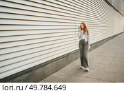 A stylish woman walks a modern sidewalk, focused on her phone, surrounded by sleek architecture. She represents leisure and individuality in trendy jeans and sneakers, enjoying the vibrant city. A relaxed and informal street style portrait of a woman captured in an urban setting. Стоковое фото, агентство Ingram Publishing / Фотобанк Лори