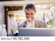 In a vibrant outdoor space, a young woman sits comfortably and happily with her laptop, joyfully reflecting her digital connection, embodying creativity, and fulfillment in her dynamic and busy life. A young woman is smiling at her laptop in a modern outdoor setting, enjoying her work. Стоковое фото, агентство Ingram Publishing / Фотобанк Лори
