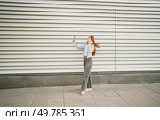 A trendy young woman with vibrant red hair joyfully takes a playful selfie in front of a beautifully textured wall, capturing a delightful moment filled with fun and creativity that defines her style. A Young Woman Happily Taking a Selfie Against a Vibrant and Modern Architectural Background. Стоковое фото, агентство Ingram Publishing / Фотобанк Лори