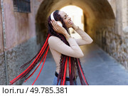 A cheerful woman with vibrant, stylish braided hair joyfully listens to music while in an urban environment, perfectly expressing her happiness and carefree spirit as she moves to the rhythm. A Joyful Woman with Beautifully Braided Hair Enjoying Music in a Lively Urban Setting. Стоковое фото, агентство Ingram Publishing / Фотобанк Лори