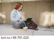 A young woman casually sits on a ledge, engrossed in her laptop. This scene perfectly embodies themes of productivity, remote work, and the contemporary lifestyles found in urban environments. A young woman working diligently on her laptop outdoors, dressed in stylish casual attire. Стоковое фото, агентство Ingram Publishing / Фотобанк Лори