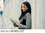 In a lively urban setting, a fashionable young woman leans against a textured wall, absorbed in her smartphone, embodying modern lifestyle and digital connections in todays fastpaced world. A young woman is engaged in using her smartphone while in a bustling urban environment. Стоковое фото, агентство Ingram Publishing / Фотобанк Лори