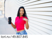 A confident woman wearing a vibrant pink crop top and stylish denim shorts poses joyfully with a refreshing drink in hand, radiating positivity and cheer against a modern and fashionable backdrop. A Confident Woman Posing with a Drink in Hand Against a Stylish Modern Background Setting. Стоковое фото, агентство Ingram Publishing / Фотобанк Лори