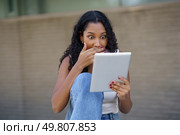 A young woman displays a reaction of surprise while using her tablet, capturing a delightful moment of joy and active engagement in a laidback outdoor setting surrounded by nature. A surprised woman enjoys content on her tablet in a relaxed setting, engaging with joy. Стоковое фото, агентство Ingram Publishing / Фотобанк Лори