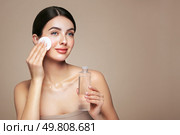 Young girl holds cotton pad while cleansing face with cosmetic milk. Skin care removal of makeup cleansing. Basic facial skin care. Стоковое фото, агентство Ingram Publishing / Фотобанк Лори