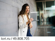 A young woman smiles brightly as she uses her tablet, dressed stylishly while leaning against a wall in an urban setting, showcasing her relaxed demeanor and enjoyment of the digital interaction. A Cheerful Woman Happily Engaging with a Digital Tablet in a Bright Modern Setting. Стоковое фото, агентство Ingram Publishing / Фотобанк Лори