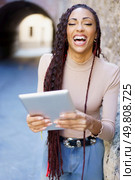 In a lively urban setting, a joyful woman in trendy casual wear is engaged with her tablet, enjoying a refreshing break from her routine and soaking in the vibrant city atmosphere. A Joyful Woman Laughs with a Tablet in a Bustling Urban Setting, Radiating Happiness. Стоковое фото, агентство Ingram Publishing / Фотобанк Лори