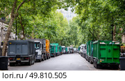 A street packed with delivery trucks and waste bins overflowing. Symbol of a major environmental problem caused by urban overconsumption waste. Abstract image. Стоковое AI-изображение, AI-художник ALLA YURTAYEVA / Фотобанк Лори