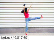 A joyful dancer leaps energetically in a stylish outfit, set against a colorful striped background that enhances her playful, dynamic movements, reflecting her excitement and happiness. Dynamic and Joyful Dance Pose Captured Against a Striped Background for a Vivid Effect. Стоковое фото, агентство Ingram Publishing / Фотобанк Лори