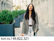 A stylish and fashionable young woman with beautifully curly hair strolls gracefully outdoors, exuding confidence and pure joy while showcasing a chic and trendy outfit against a modern city backdrop. A Stylish Young Woman Smiling Happily Outdoors in a Vibrant Urban Setting Full of Life. Стоковое фото, агентство Ingram Publishing / Фотобанк Лори
