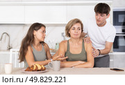 Sad mom sits silently in kitchen, adult children, guy and girl sympathize and comfort woman. Стоковое фото, фотограф Яков Филимонов / Фотобанк Лори