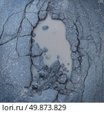 Pot hole or pothole image of a broken cracked asphalt pavement with a dirty water puddle as a transportation symbol of road maintenance and the car insurance risk to auto suspensions. Стоковое фото, агентство Ingram Publishing / Фотобанк Лори