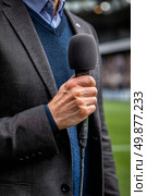 Sports Commentator Holds Microphone While Preparing for Match Commentary at Stadium. Стоковое AI-изображение, AI-художник Юлия Гапеенко / Фотобанк Лори