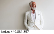 Elegant older man in white suit poses against neutral wall, showcasing sophistication and timeless style during daytime. Стоковое AI-изображение, AI-художник Сергей Толмачёв / Фотобанк Лори