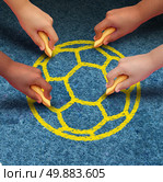 Community soccer concept as a group of hands representing ethnic groups of young people from many world nations holding chalk cooperating together as friends to draw a yellow ball as a symbol of global sport partnership and teamwork.. Стоковое фото, агентство Ingram Publishing / Фотобанк Лори