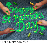 Happy Saint Patricks day concept as a group of diverse people coming together drawing green St Patrick day text with chalk as a spring time traditional Irish pride celebration symbol. Стоковое фото, агентство Ingram Publishing / Фотобанк Лори
