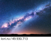 Milky Way. Fantastic night landscape with purple milky way, sky full of stars, yellow light and hills. Shiny stars. Beautiful scene with universe. Space background with starry sky. Astrophotography. Стоковое фото, агентство Ingram Publishing / Фотобанк Лори
