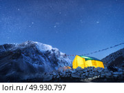 Yellow glowing tent against high rocks with snowy peak and sky with stars at night in Nepal. The Himalayan Mountains. Landscape with mountains, starry sky and bivouac. Trekking in Himalayas. Travel. Стоковое фото, агентство Ingram Publishing / Фотобанк Лори