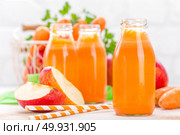 Fresh carrot and apple juice on white background. Carrot and apple juice in glass bottles on white table, closeup. Стоковое фото, агентство Ingram Publishing / Фотобанк Лори