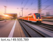 High speed red train with motion blur effect on the railway stat. High speed red train with motion blur effect on the railway station at sunset. Landscape. Modern intercity passenger train in motion on the railway platform at dusk. Commuter vehicle on railroad. Стоковое фото, агентство Ingram Publishing / Фотобанк Лори