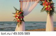 Romantic beach sunset wedding arch with flowing white drapes and vibrant flowers. Стоковое AI-видео, аниматор Владимир Федоров / Фотобанк Лори