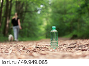 Бутылка воды на лесной тропе, удаляющаяся женщина с собакой на фоне, размыта. Стоковое фото, фотограф Евгений Ковальский / Фотобанк Лори