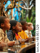 A row of attentive children watching intently, captivated by a presentation or exhibit, demonstrating eagerness and curiosity. Стоковое AI-изображение, AI-художник Данила Большаков / Фотобанк Лори