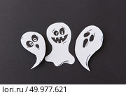 Decorative application from flying singing ghosts and spirit, smiling on a black paper background, place under text. Halloween concept. Top view.. Halloween party card with paper handmade laughing flying scary specters, spirits on a black background. Стоковое фото, агентство Ingram Publishing / Фотобанк Лори