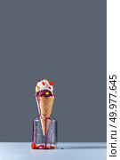 The waffle cone with a ball of milk ice cream with red and yellow capsules and lollipops on a gray background with a place under the text. The concept of summer catarrhal diseases and their treatment.. A balls of cold dessert in a waffle cone with red and yellow pills and a lollipop stands in a glass jar on a dark gray background on the table. Pils and lollipops in a jar. Copy space. Стоковое фото, агентство Ingram Publishing / Фотобанк Лори