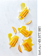 Food pattern from splashes of melting fruit ice cream on a stick of ice and peach slices on a gray marble background with copy space. Layout for your ideas. Flat lay. Composition of juicy pieces of peach, ice and melting ice cream on a stick with splashes on a gray marble table with copy space. Flat lay. Стоковое фото, агентство Ingram Publishing / Фотобанк Лори