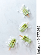 Green ice cream on a stick with a slice of fresh kiwi and ice, presented in the form of a corner frame on a gray marble background with a copy of the space. Layout for your ideas. Flat lay. Composition in the form of a corner frame of ice cream on a stick with a piece of kiwi and ice on a gray marble background. Space for text. Flat lay. Стоковое фото, агентство Ingram Publishing / Фотобанк Лори