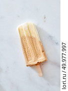 Creme brulee coffee ice cream on a wooden stick over marble background, top view. Healthy summer dessert. Frozen coffee gelato ice cream on a wooden stick over marble background, top view. Summer delicious desserts. Стоковое фото, агентство Ingram Publishing / Фотобанк Лори