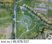 Birds eye view from the drone to a labyrinth of cut bushes, alleys, yards in the garden in the summer day at sunset.. Panoramic view from the drone to a part of botanical garden with with a labyrinth, trees, flower beds with flowers. Стоковое фото, агентство Ingram Publishing / Фотобанк Лори