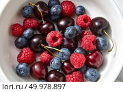 Sweet berries background from red ripe berries in ceramic plate Concept of natural organic healthy food. Top view.. Close-up of ripe sweet fruits - cherry, raspberry, blueberries in the white plate on a gray stone background. Стоковое фото, агентство Ingram Publishing / Фотобанк Лори