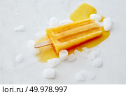 Orange melting ice cream lolly with ice slices on a gray marble table with a copy of the space. The concept of summer dessert.Flat lay. Orange fruit ice cream on a stick with slices of ice on a gray marble background with space for text. Flat lay. Стоковое фото, агентство Ingram Publishing / Фотобанк Лори