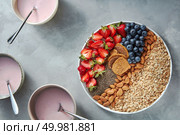 Granola, halves of strawberries, almonds, chia seeds, blueberries. Yogurt in a plate with a spoon on a gray concrete background. Ingredients for healthy breakfast. Top view. Granola, berries, nuts, chia and yogurt in a plate on a gray concrete background. Ingredients for breakfast. Top view. Стоковое фото, агентство Ingram Publishing / Фотобанк Лори