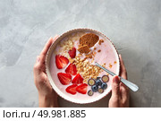 The woman’s hands hold a plate with a freshly prepared breakfast of yogurt, granola, strawberries and blueberries on a gray concrete background. Top view. The girl’s hands hold a plate of yoghurt, granola and berries on a gray concrete background. Top view. Стоковое фото, агентство Ingram Publishing / Фотобанк Лори