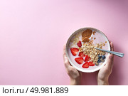 Healthy smoothie in white bowl with natural fruits, oat flakes and biscuits with woman’s hands holding a bowl on pink background. Superfoods, natural detox, diet and healthy food. Flat lay. Woman’s hands holding a bowl of organic yogurt smoothie with strawberries, banana, blueberry, oat flakes and biscuits on pink background. Flat lay. Стоковое фото, агентство Ingram Publishing / Фотобанк Лори