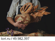 The baker’s hands hold many different kinds of bread near a wooden table with dried flowers. Variety of bread hold men’s hands. Стоковое фото, агентство Ingram Publishing / Фотобанк Лори