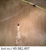 Aerial view of the tractor plowing spring field, a column of dust stretches behind the tractor, Ukraine. Photo from the drone. Aerial view tractor with a cultivator for seeds at the beginning of the spring season of agricultural work. Стоковое фото, агентство Ingram Publishing / Фотобанк Лори