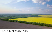 Panoramic view of fields with rapeseed and cultivated fields, a small village with a river in the distance against the blue sky. Photo from the drone. Panoramic view of a field and a village in the distance against a blue sky. Photo from the drone. Стоковое фото, агентство Ingram Publishing / Фотобанк Лори