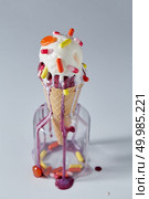The waffle cone with a cold ice cream stands in glass jar with red and yellow capsules and lollipop, gray background. The concept of summer catarrhal diseases and their treatment with place for text.. A balls ice cream in a waffle cone with red and yellow tablets and lollipops stands in a glass jar on a gray table. Pils and lollipops in a jar. Стоковое фото, агентство Ingram Publishing / Фотобанк Лори