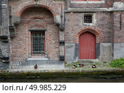 The old building with the Red door and a window on the water channel. Typical architecture of Bruges, Belgium.. Red door and window at water canal,panoramic view. Стоковое фото, агентство Ingram Publishing / Фотобанк Лори