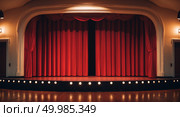 Classic theater stage with vibrant red curtain and elegant proscenium in anticipatory atmosphere before performance. Стоковое AI-изображение, AI-художник Андрей Бакусов / Фотобанк Лори