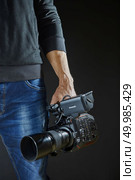 Kiev, Ukraine - April 22, 2018: Cameraman holding his professional camcorder Panasonic AU-EVA1 in the studio. Operator in social environment, filming, news outlet, motion-picture cameraman. Kiev, Ukraine - April 22, 2018: Photographer and video maker man hold Panasonic AU-EVA1 video camera on his hand to making footage. Редакционное фото, агентство Ingram Publishing / Фотобанк Лори