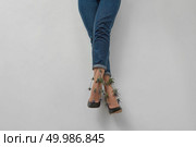 Flowers eryngium with woman legs in blue jeans on a gray background with copy space.. Woman legs with flowers eryngium in blue trousers on a gray. Стоковое фото, агентство Ingram Publishing / Фотобанк Лори